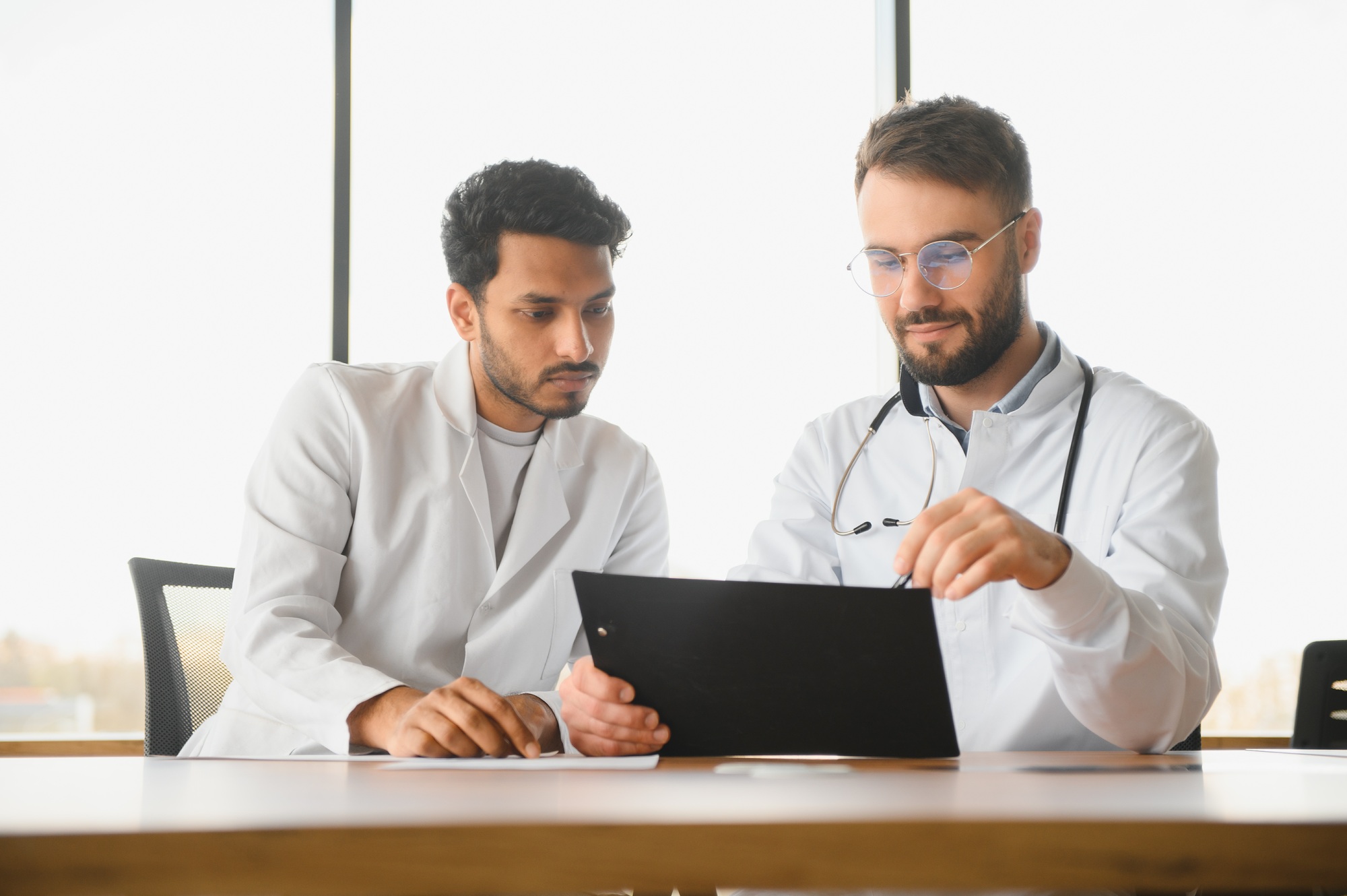 An Indian doctor and a European doctor stand together in a hospital lobby
