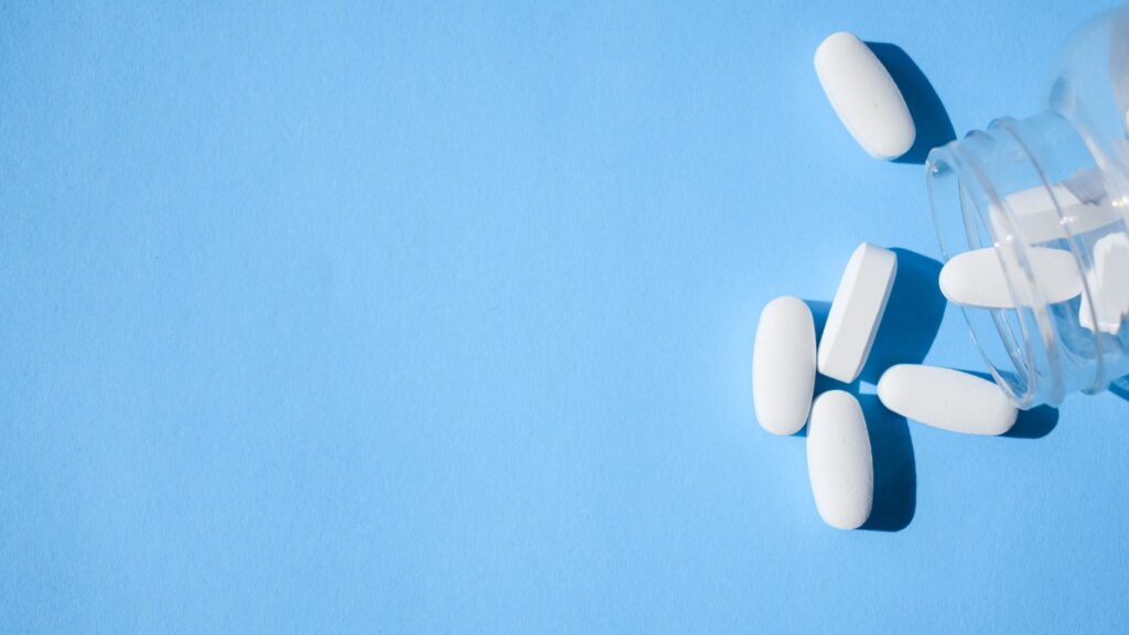 Oxycodone pills. Opioid pain medication, narcotic. Close up white pills with a bottle on a blue