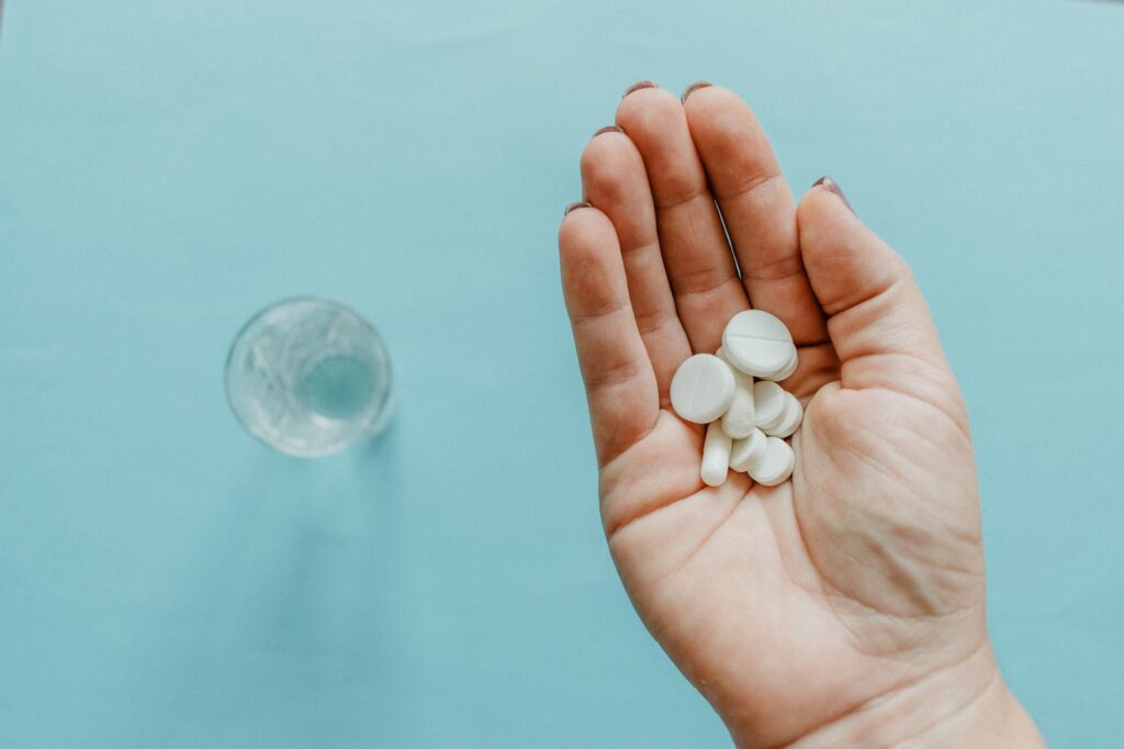 Sleeping Pills, Prescription Drugs. White pills in female palm and glass of water on blue background