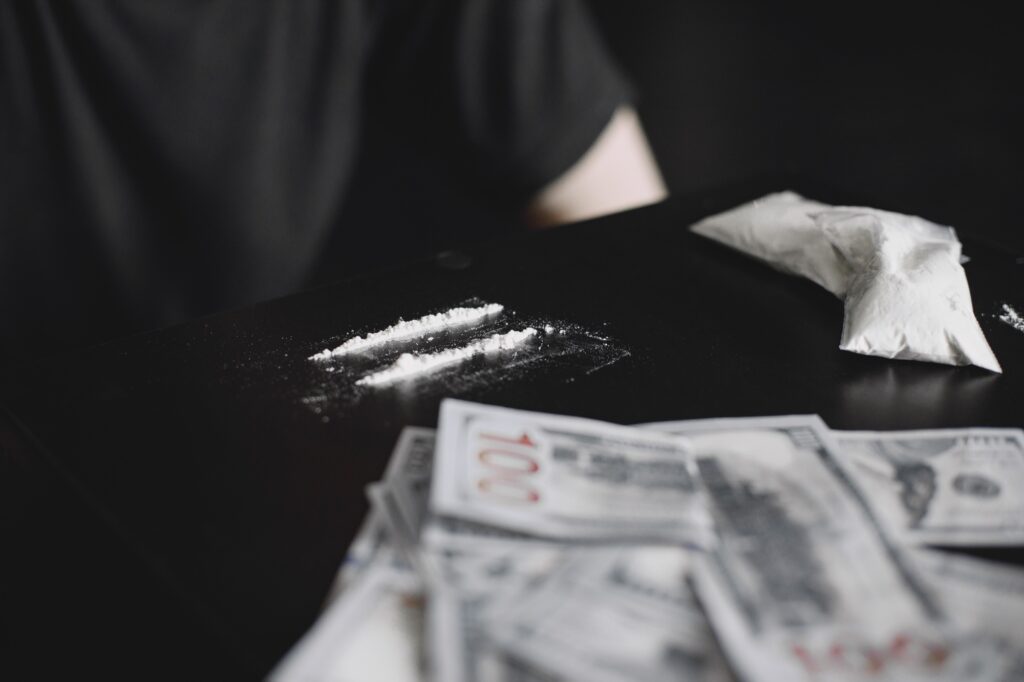 Young addicted man taking cocaine with dollar