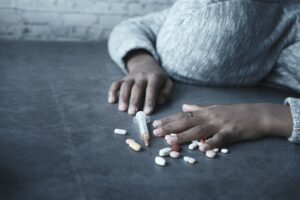 drug addiction concept with hand holding pills and syringe laying on floor