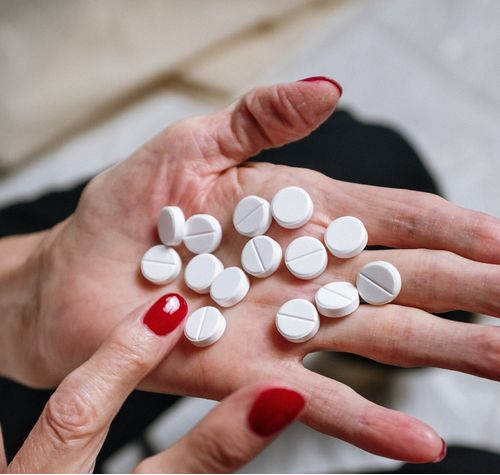 An image of a hand with red nail polish holding white pills.
